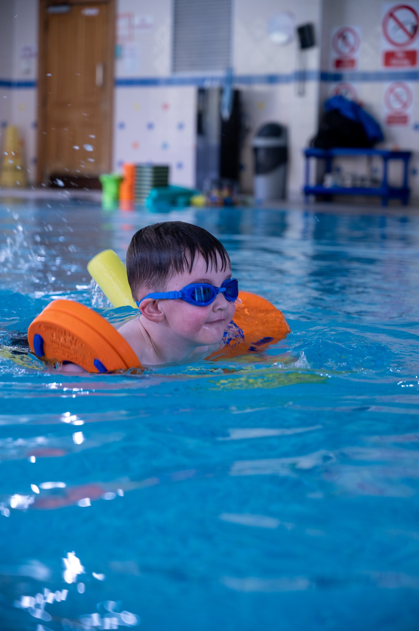 A young swimmer in blue goggles practising with orange buoyancy aids