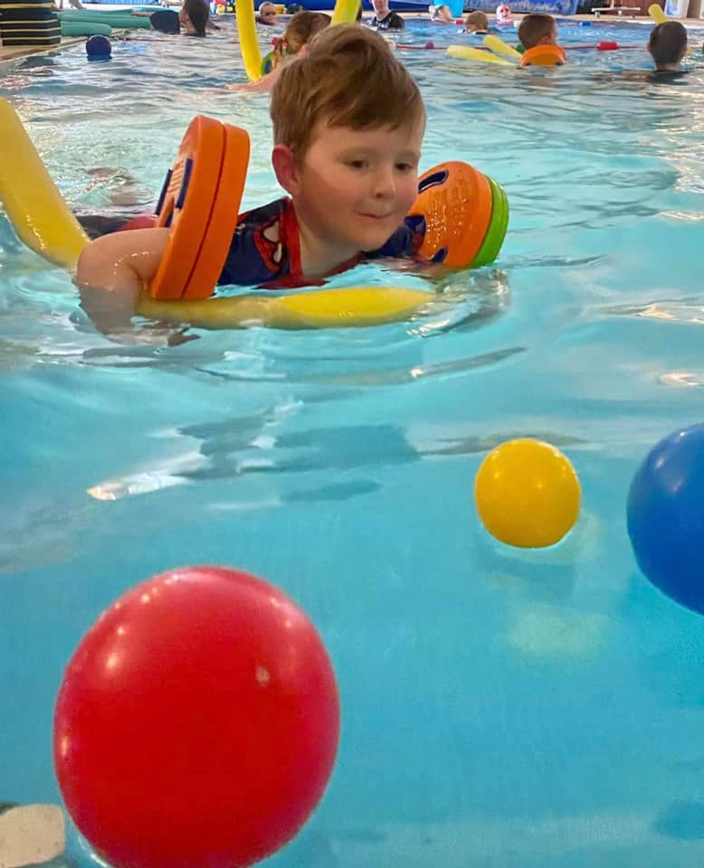 A young swimmer practising with a kickboard and colourful floating balls