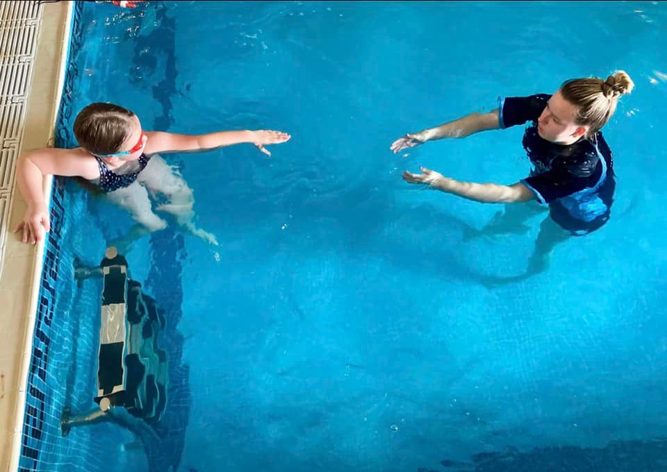 A swimming teacher encouraging a child to reach out from the poolside