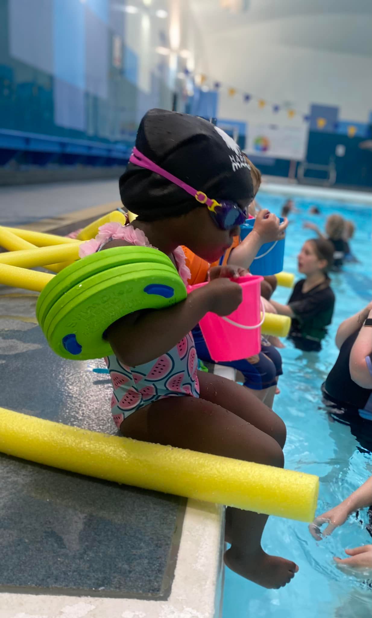 A young swimmer with goggles and colourful floats at the poolside