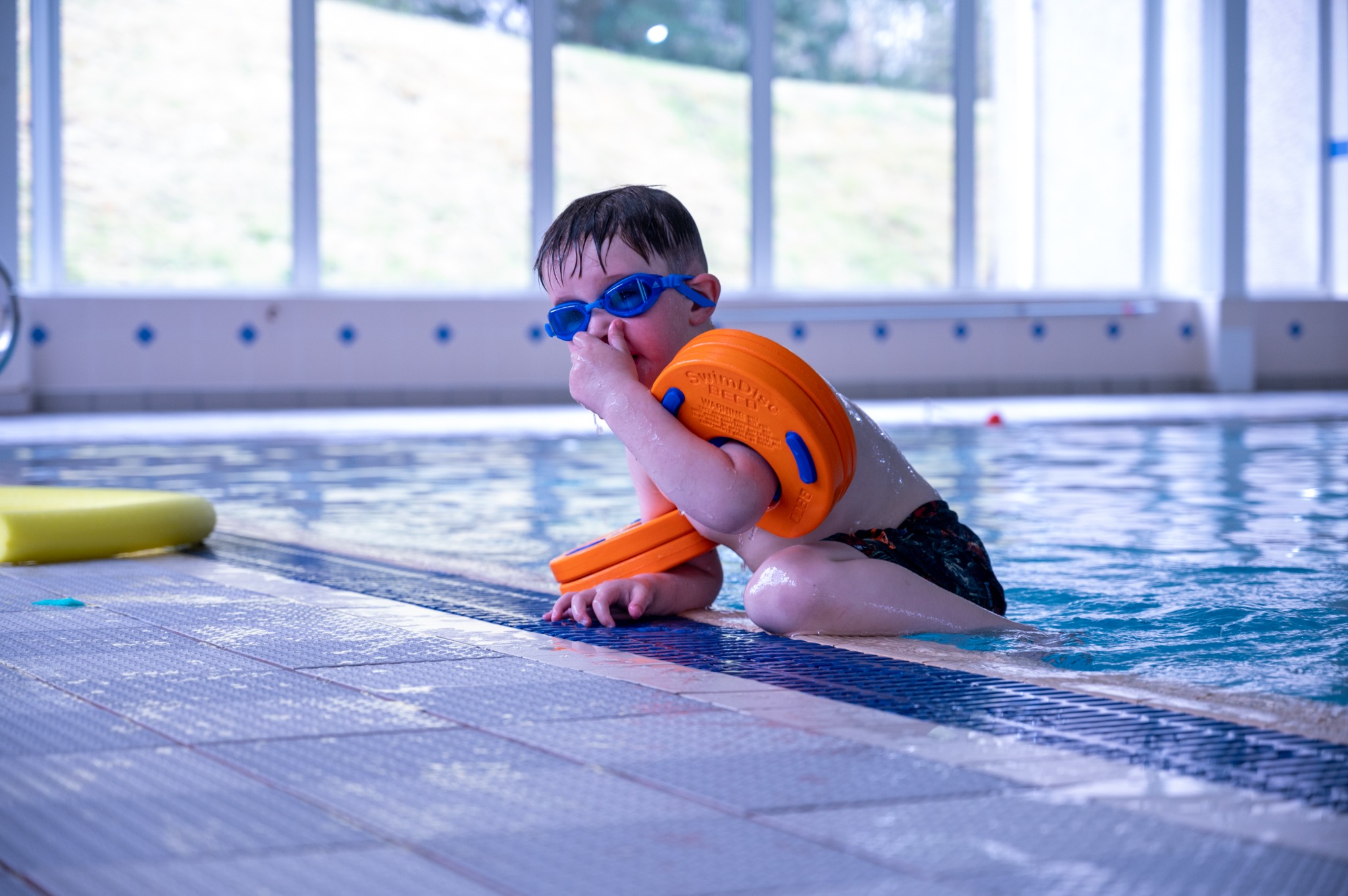 A swimmer in goggles and buoyancy aids gets ready at the pool edge